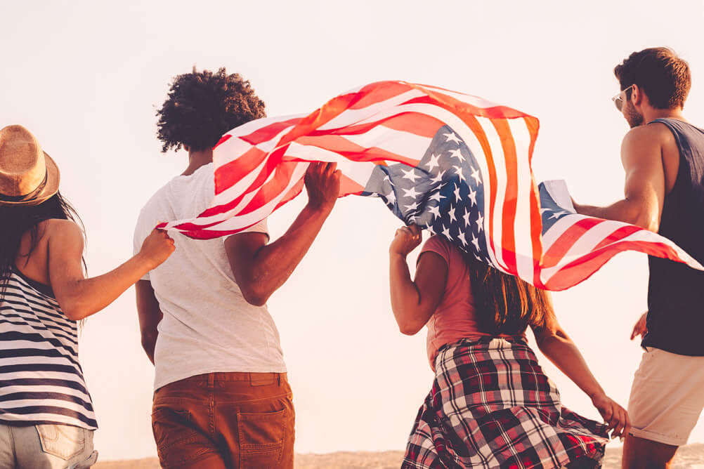 4 personas caminan sosteniendo la bandera de Estados Unidos