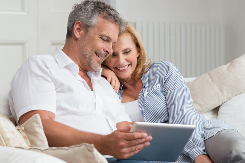 Una pareja está sentada en un sofa mientras usan una tablet