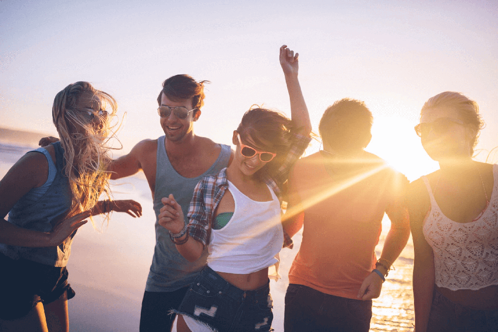 Grupo de  amigos felices en la playa con el atardecer de fondo